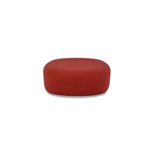 A red silicone lid with the 'Aeropress' brand name embossed on the top surface.