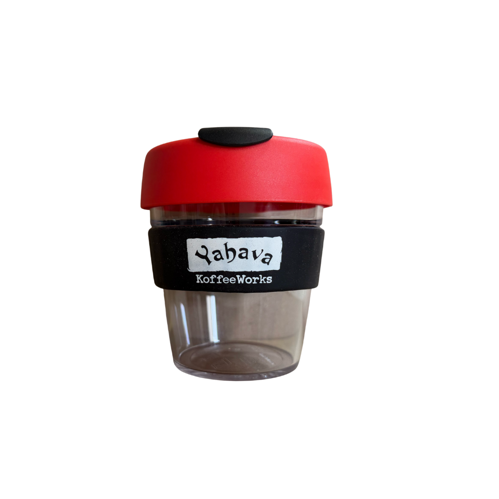 A reusable coffee cup with a bright red lid, a black silicone sleeve featuring the 'Yahava KoffeeWorks' logo, and a clear plastic body, shown on a plain white background.