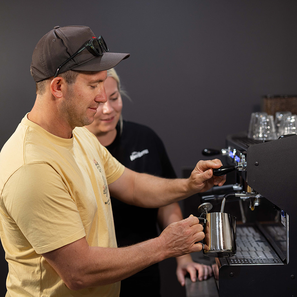Man operating a coffee machine with a woman in the background