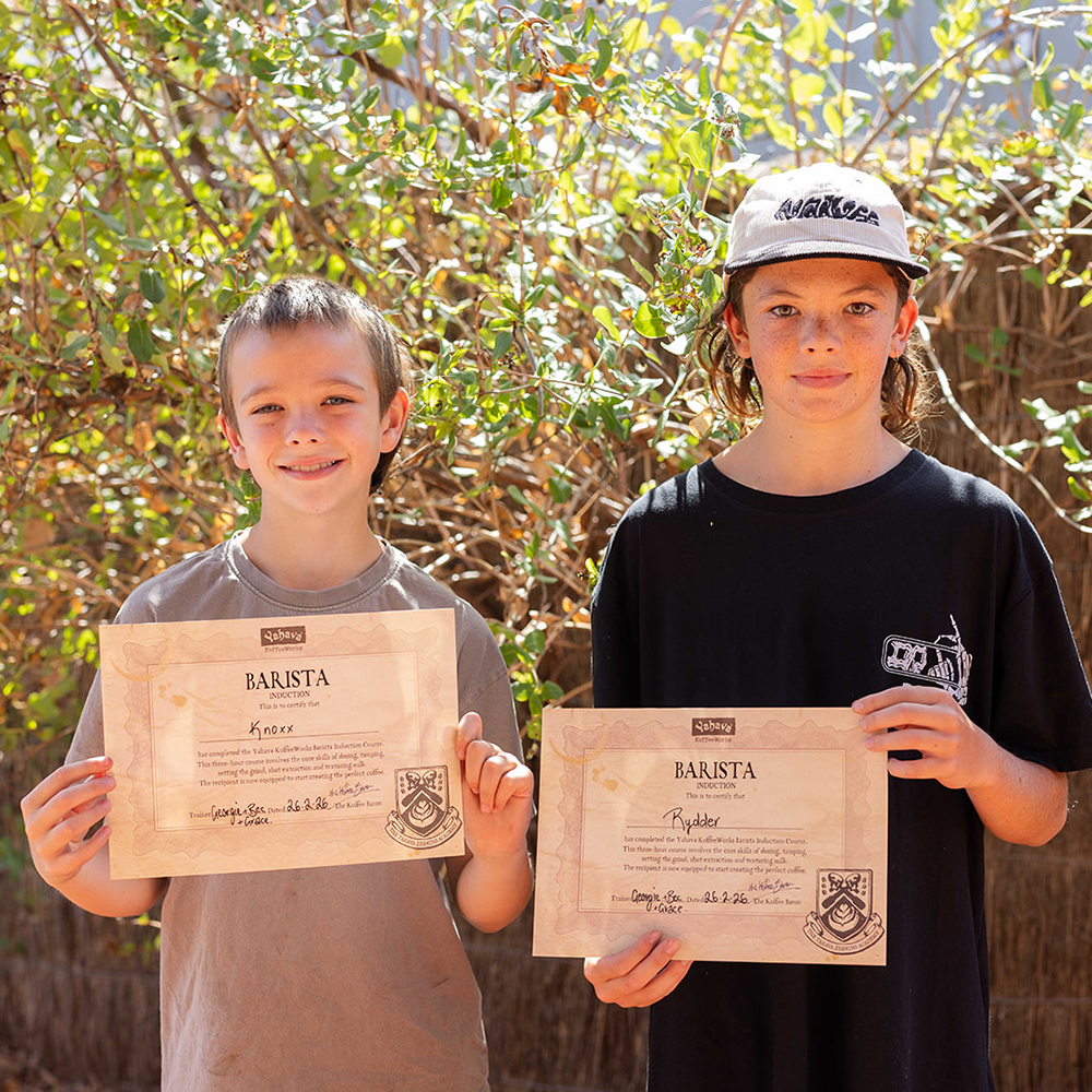 Two children holding certificates outdoors with greenery in the background